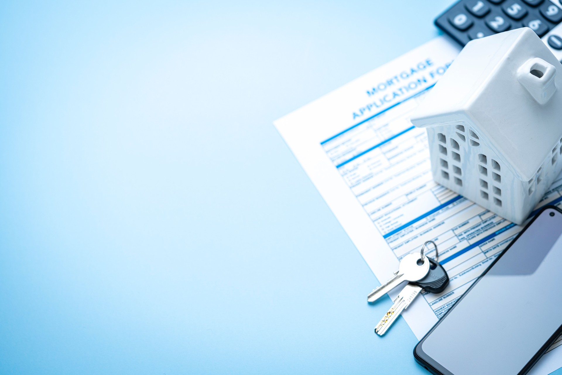 Flat lay of real estate concept. Mortgage application form, house model, house keys and mobile phone with blank screen. Copy space